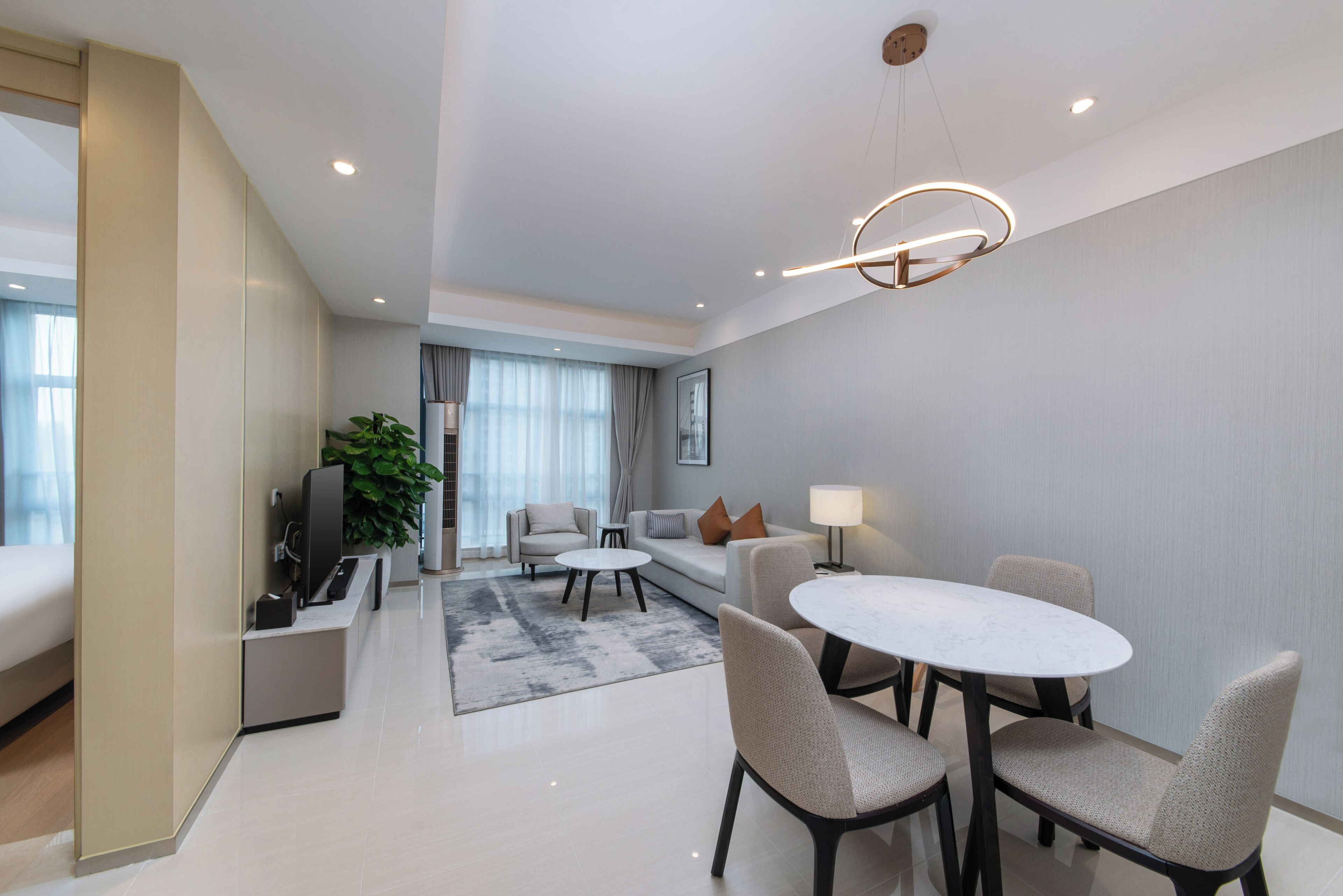 A modern hotel room with a dining area, a sofa, a TV, and a plant.