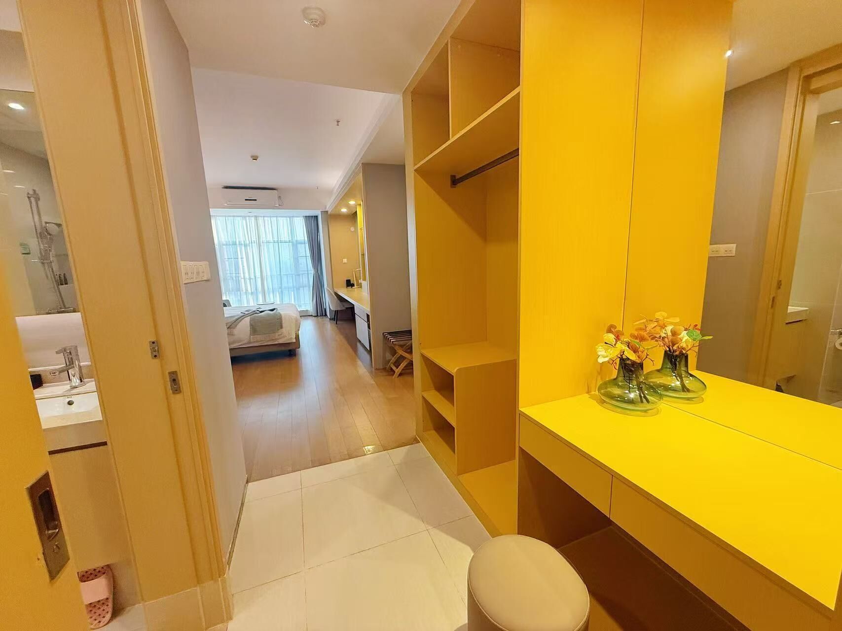 A hotel room with a yellow vanity, a bed, a desk, and a bathroom with a sink and mirror.