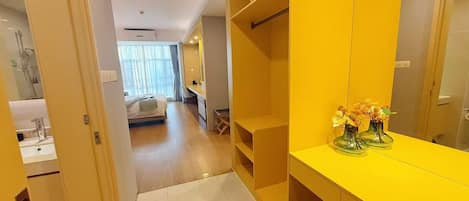 A hotel room with a yellow vanity, a bed, a desk, and a bathroom with a sink and mirror.