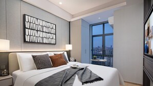 Habitación de hotel moderna con una cama grande, vistas a la ciudad y una obra de arte contemporánea sobre la cama.