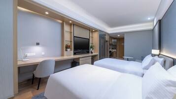Habitación de hotel con dos camas, un escritorio con computadora, un televisor y una pequeña mesa con lámpara.