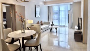 Habitación de hotel moderna con zona de comedor, sofá, mesa de centro y un amplio ventanal con cortinas.