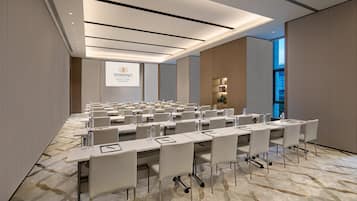 A conference room with multiple tables and chairs, a large screen displaying the Somerset logo, and a patterned carpet.