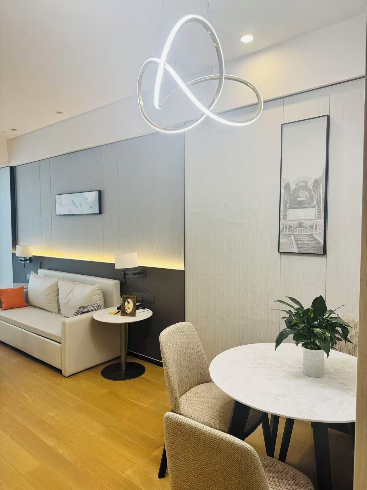 Un salon moderne avec un canapé, une table ronde entourée de chaises, une petite table ronde avec une lampe et une plante en pot.