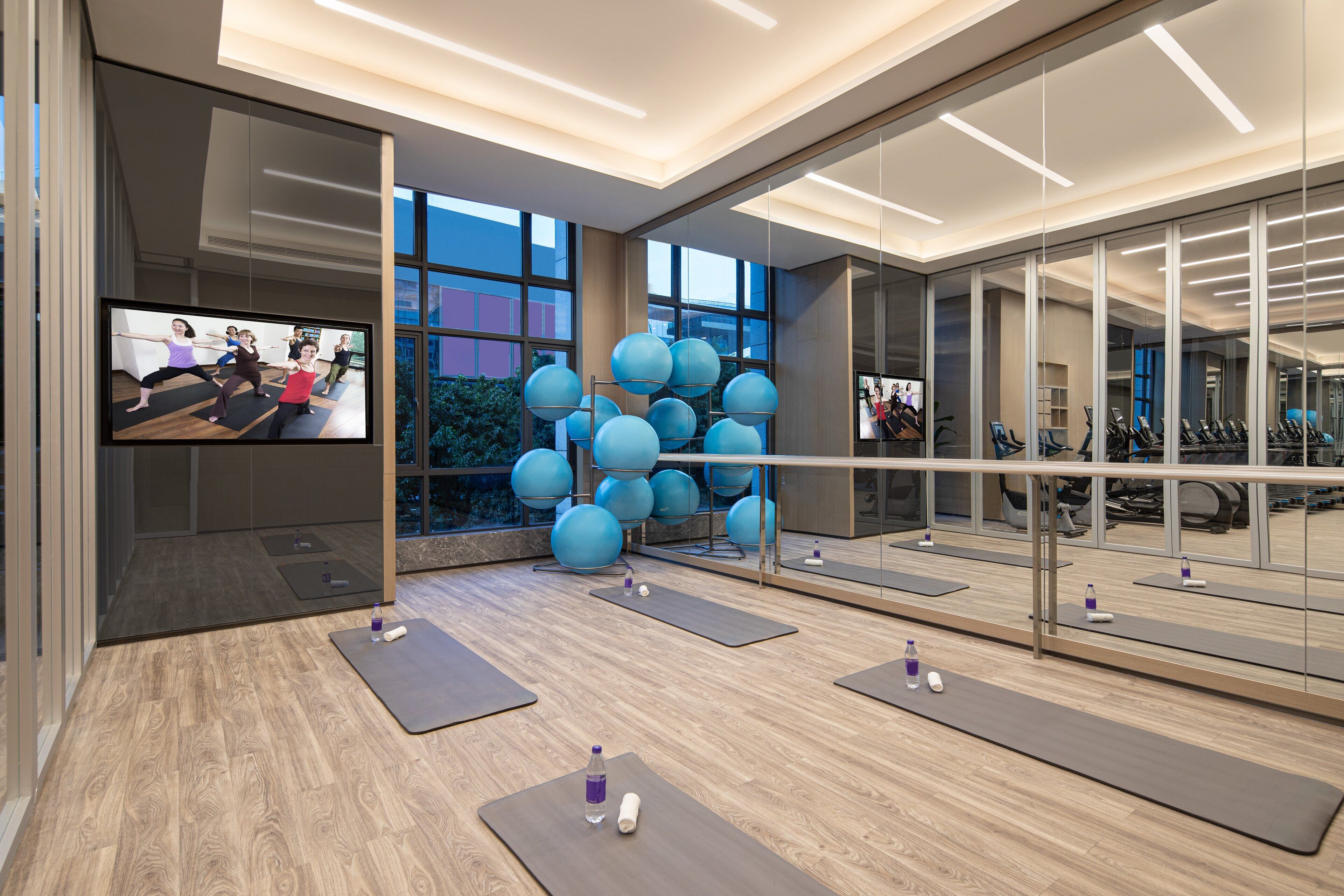A modern gym with exercise equipment, large windows, and a mirrored wall.