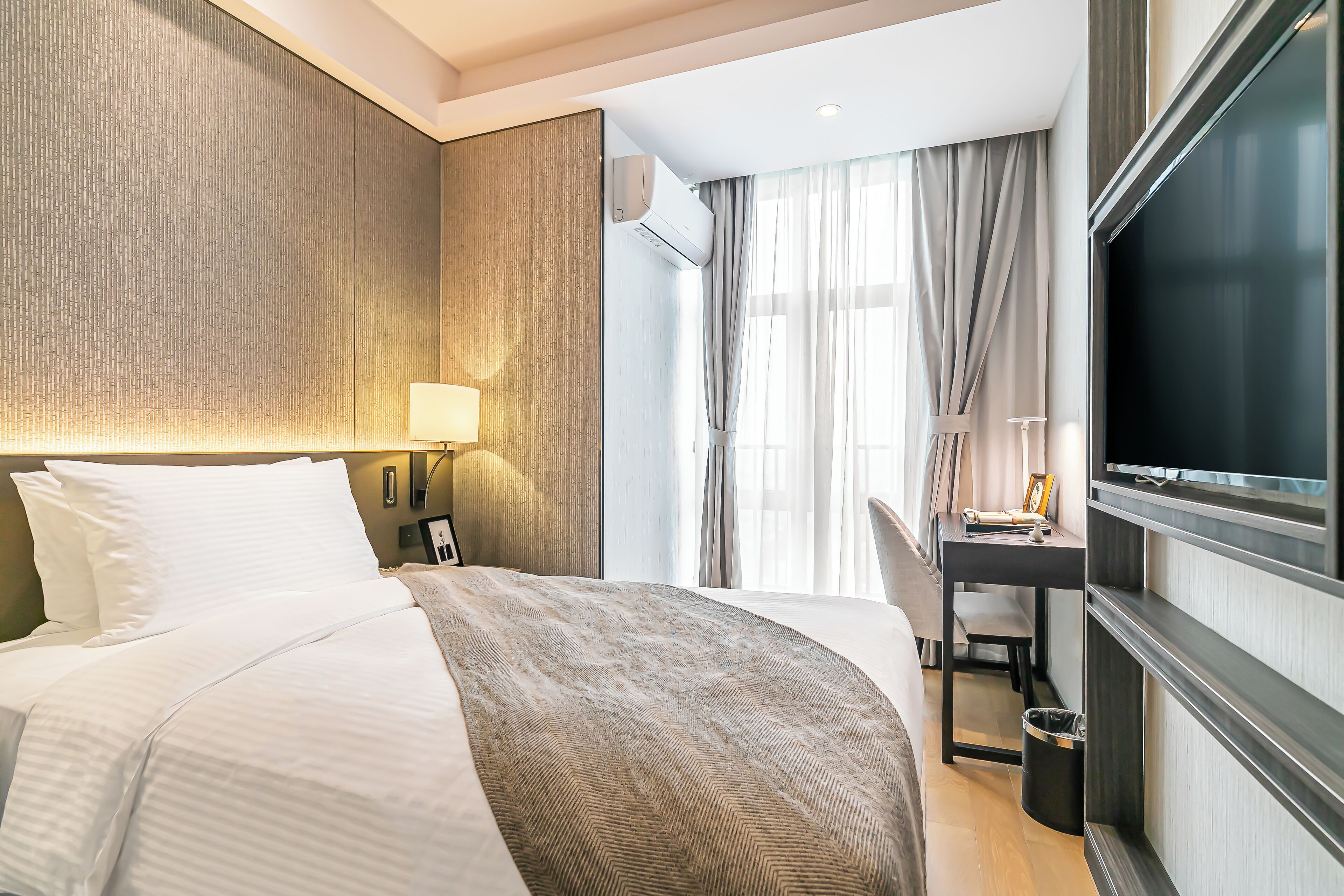 A hotel room with a bed, a desk, a TV, and a window with curtains.