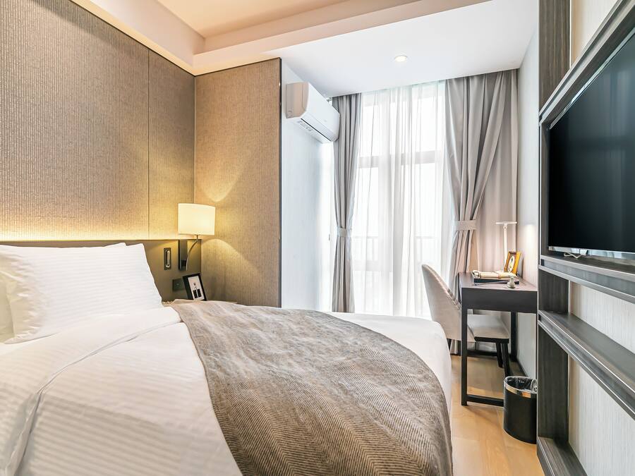 Habitación de hotel con cama, escritorio, televisión y ventana con cortinas.