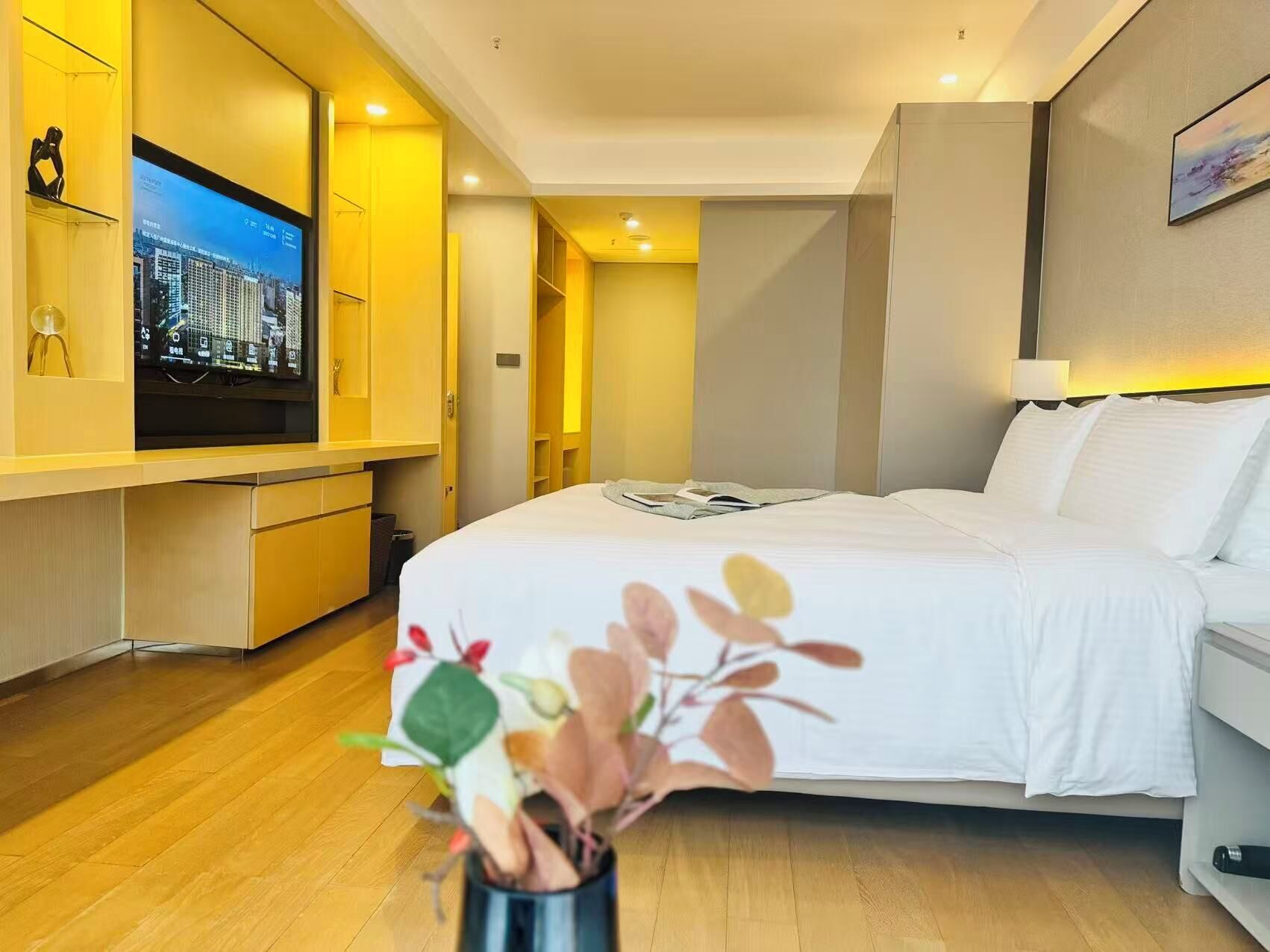 A hotel room with a bed, a TV, a desk, and a plant.