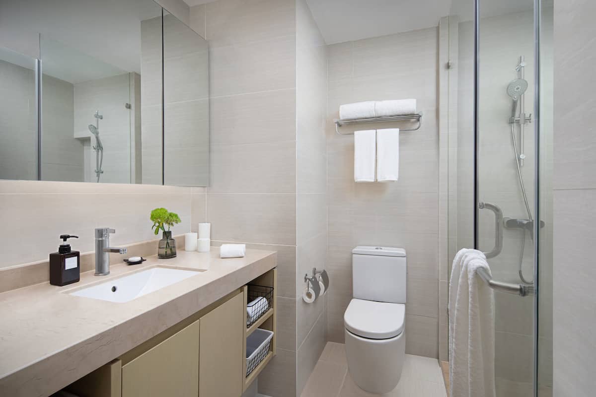 Un baño moderno con un espejo grande, un lavamanos, un inodoro y una ducha con mampara de vidrio.