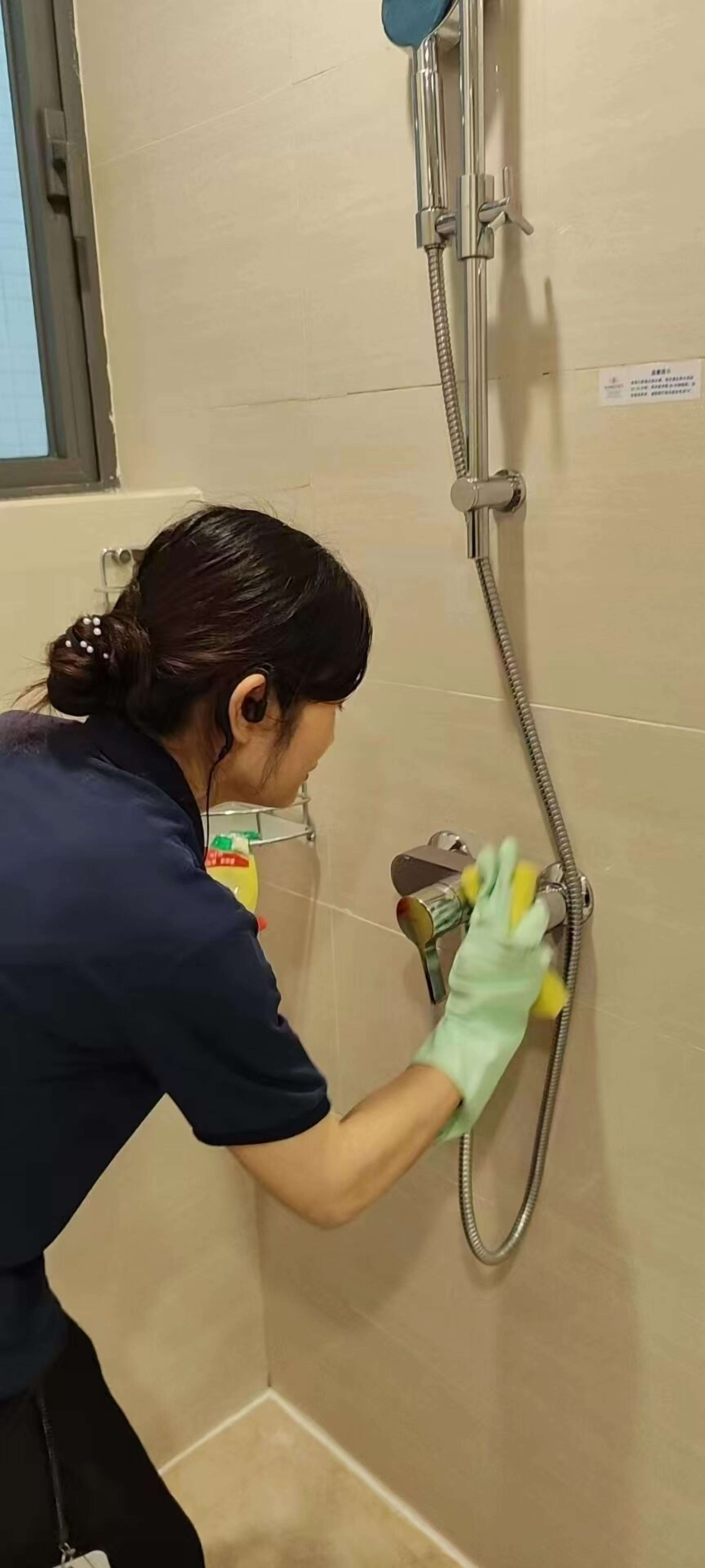 Una persona limpiando una zona de ducha en un baño.