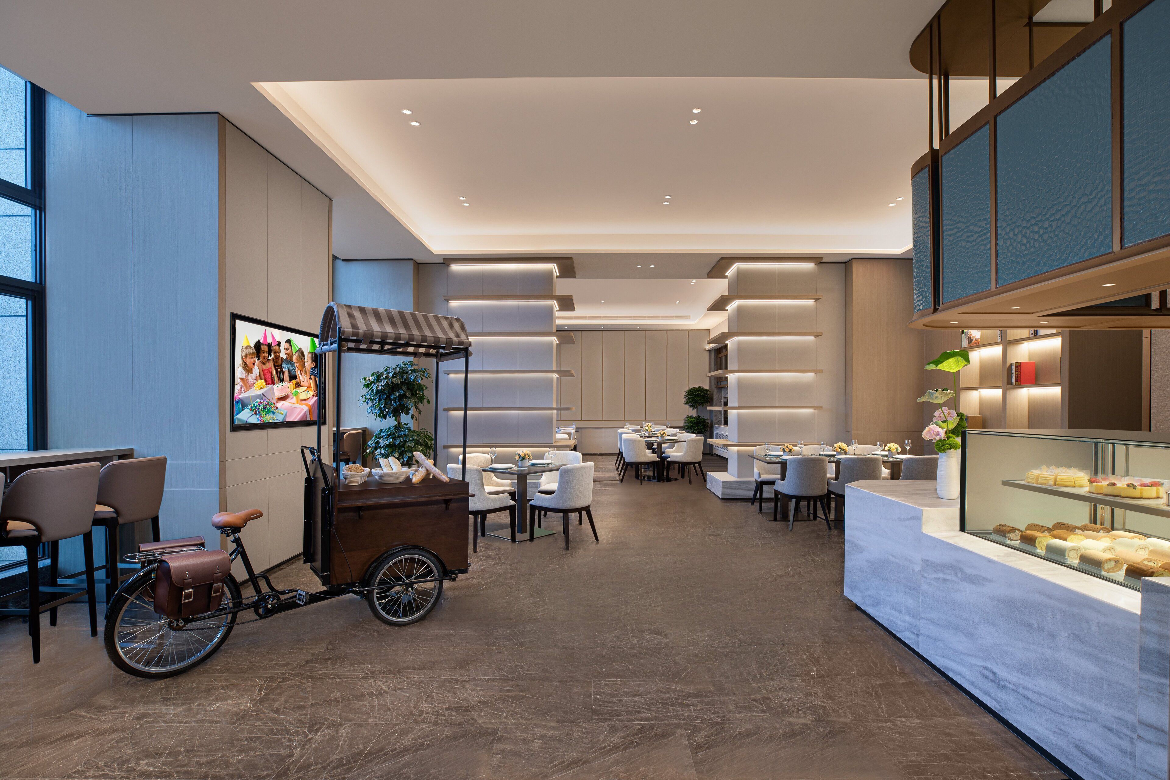 Een moderne hotel lobby met een zithoek, een etalage met eten en een fietskar.