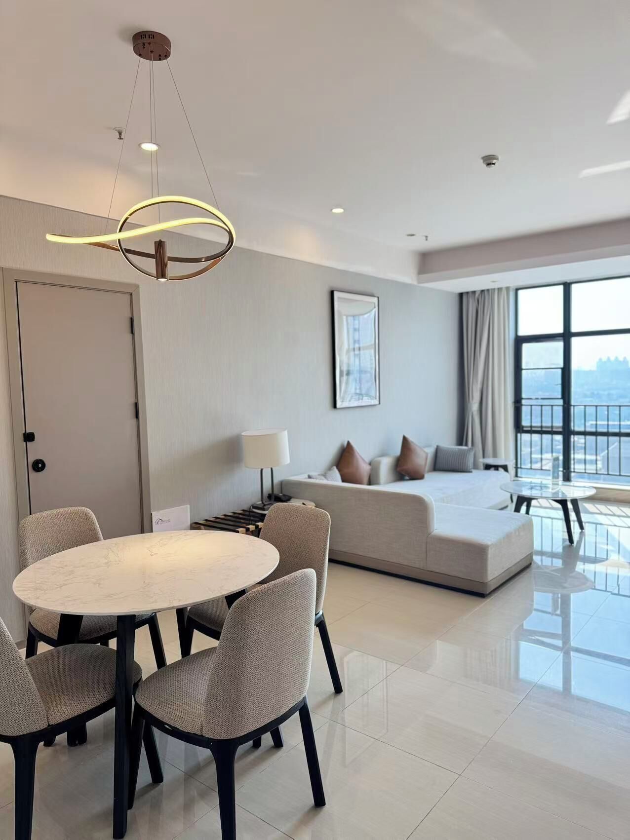 A modern hotel room with a dining area, a sofa, and a large window offering a view.