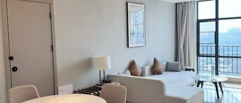 A modern hotel room with a dining area, a sofa, and a large window offering a view.