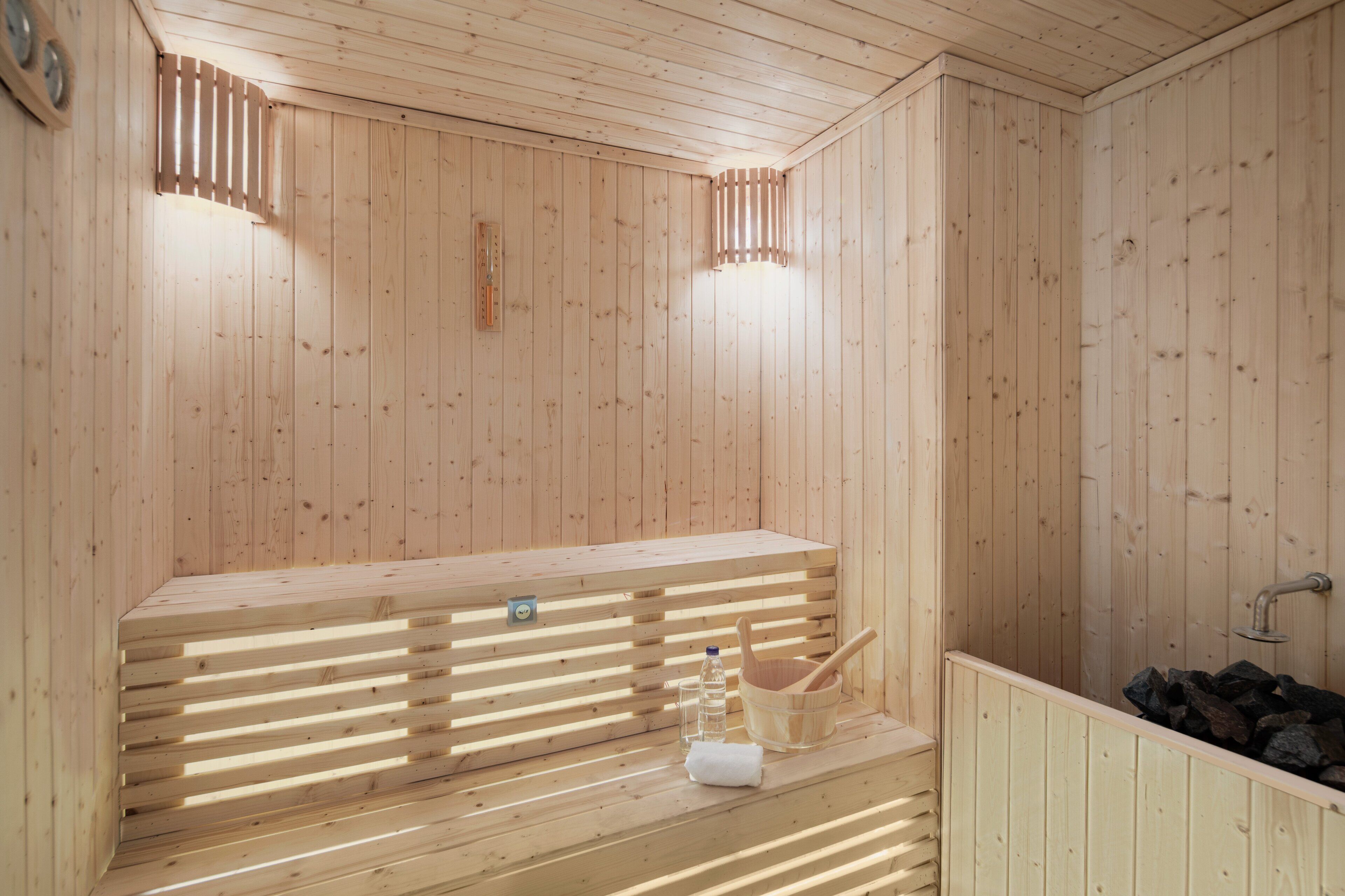 A wooden sauna with a bench, a bucket, a towel, and a water bottle.
