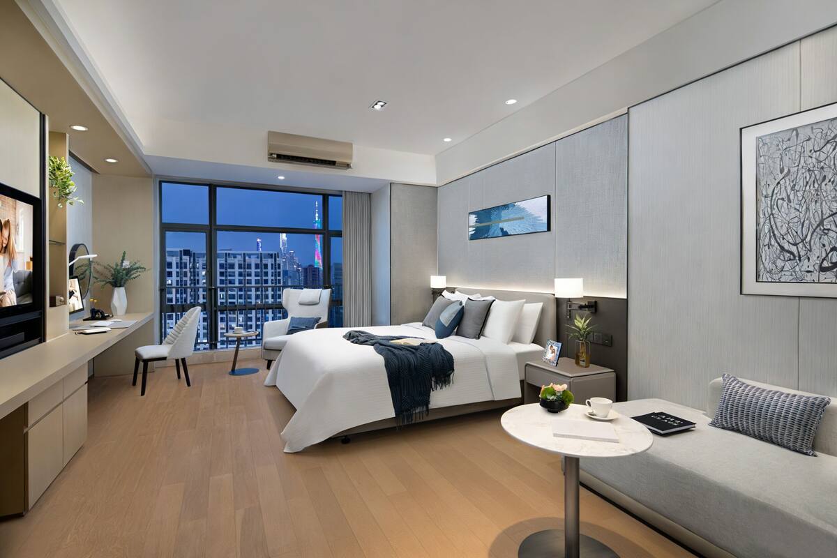 Habitación de hotel moderna con una cama grande, un sofá, un escritorio y vistas a la ciudad.