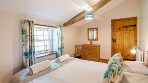 A bedroom with a large bed, a wooden dresser, a mirror, and a window with curtains. - Dudmire (Appleby-in-Westmorland)