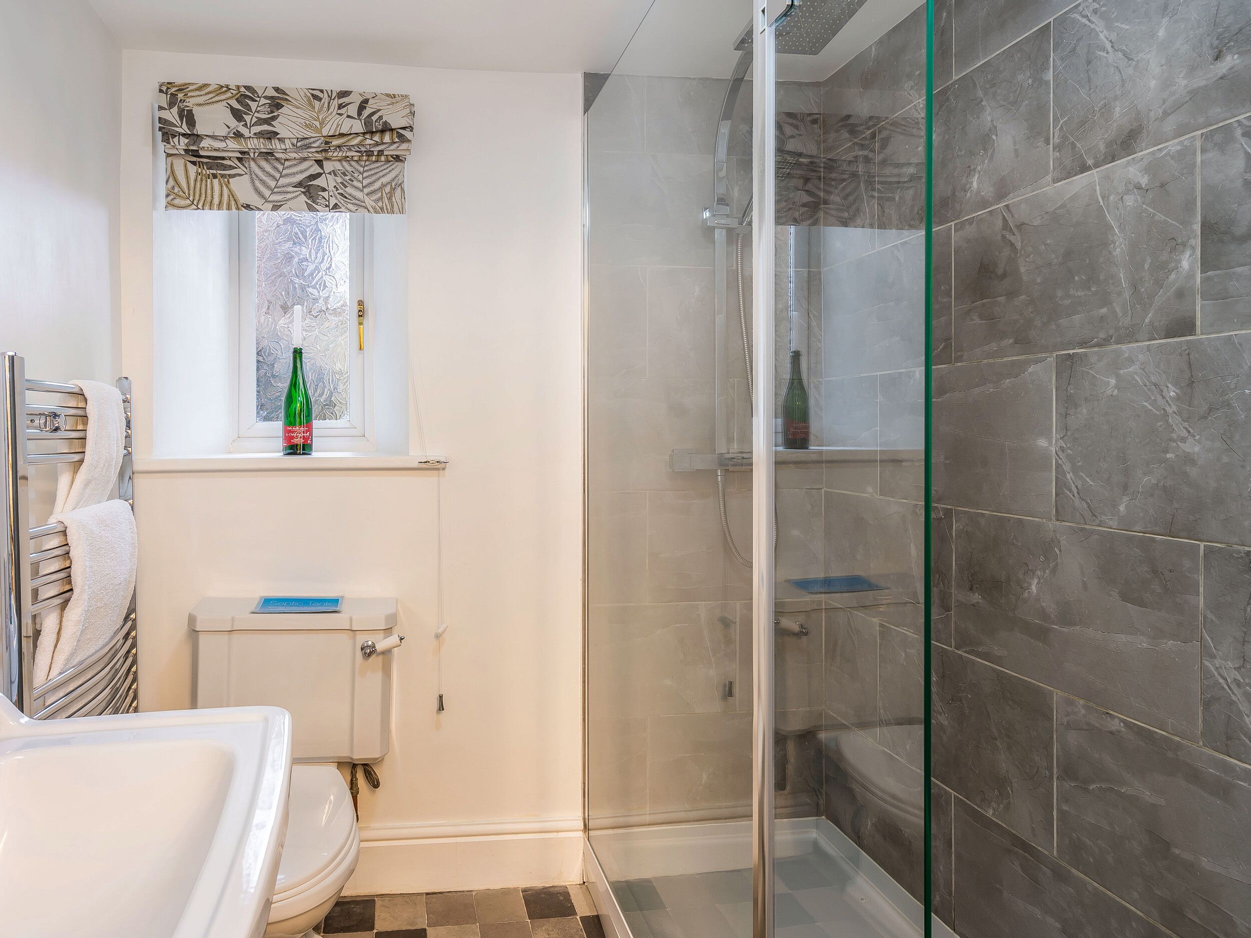 A bathroom with a toilet, a shower enclosure, and a window with a curtain.