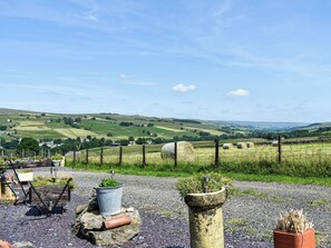A rural landscape with rolling hills, a stone wall, and hay bales in the foreground.