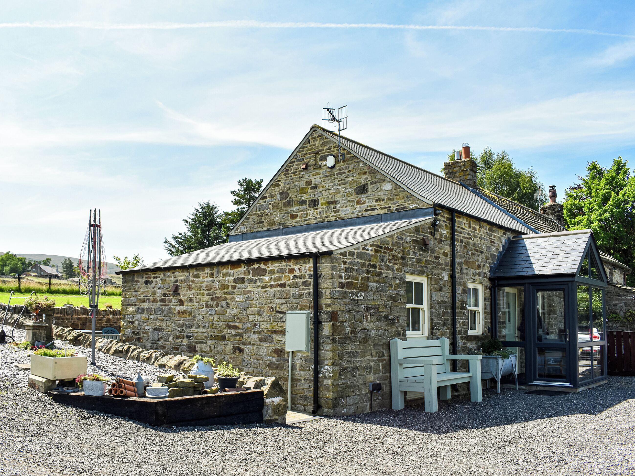A stone building with a sloped roof, a small porch, and a gravel driveway.