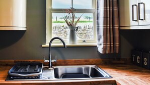 A kitchen with a built-in sink, a window with a view of a stone wall and greenery, and a vase with branches. - 2 bedroom accommodation in Westgate, Near Stanhope (Westgate, Near Stanhope)