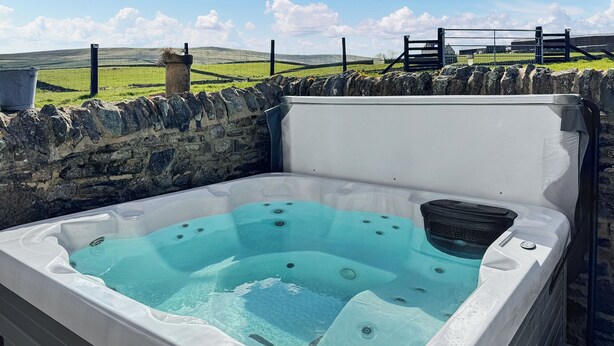 A hot tub with a stone wall backdrop and a grassy field in the background. - 2 bedroom accommodation in Westgate, Near Stanhope (Westgate, Near Stanhope)