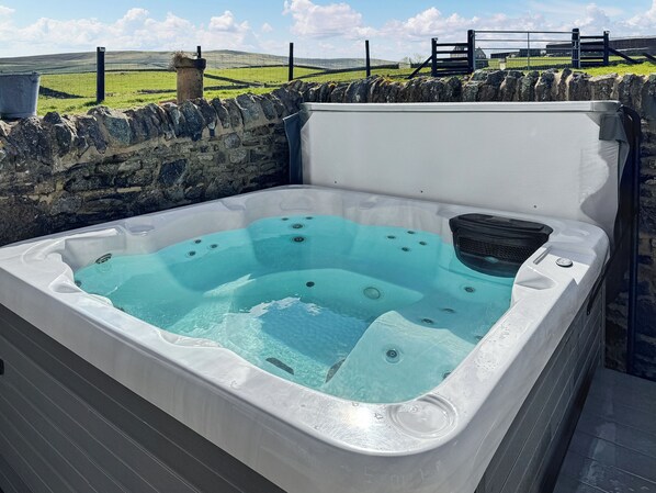 A hot tub with a stone wall backdrop and a grassy field in the background.