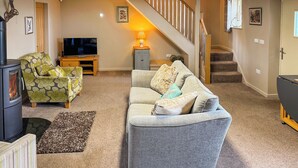 A cozy living room with a sofa, armchair, and a fireplace. A staircase leads to an upper level. - 2 bedroom accommodation in Westgate, Near Stanhope (Westgate, Near Stanhope)
