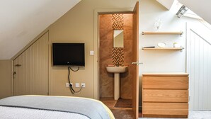 A bedroom with a bed, a TV mounted on the wall, a wooden dresser, and a bathroom with a sink and mirror. - 2 bedroom accommodation in Westgate, Near Stanhope (Westgate, Near Stanhope)