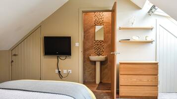 A bedroom with a bed, a TV mounted on the wall, a wooden dresser, and a bathroom with a sink and mirror.