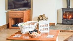 Una sala de estar con un televisor sobre un mueble de madera, una chimenea y una mesa con cestas de pan y aperitivos.