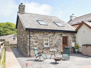 Ein Steinhaus mit Ziegeldach, eine kleine Veranda mit zwei Stühlen, einem Tisch und einem Grill.