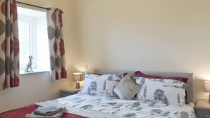 Een net opgemaakt bed met beddengoed met een patroon, een raam met gordijnen en nachtlampjes.