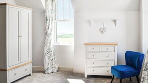 A bedroom with a wardrobe, a chest of drawers, a blue chair, and a window with a view of the outdoors. - 4 bedroom accommodation in Annan (Annan)