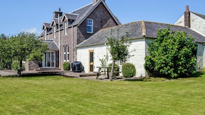 A two-story house with a stone facade, a large lawn, and a small garden area with a bench and a picnic table. - 4 bedroom accommodation in Annan (Annan)