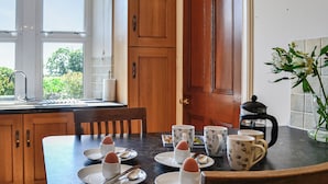 A kitchen with wooden cabinets, a marble countertop, and a dining table set with plates, cups, and a coffee pot. - 4 bedroom accommodation in Annan (Annan)