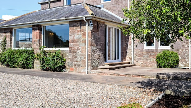 A two-story stone house with a large bay window, a covered porch, and a gravel driveway. - 4 bedroom accommodation in Annan (Annan)