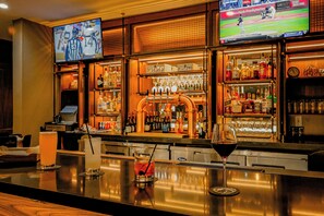 A bar area with a television displaying a baseball game, a well-stocked liquor shelf, and a few glasses of drinks on the counter. - Four Points BY Sheraton Austin Airport (Austin)