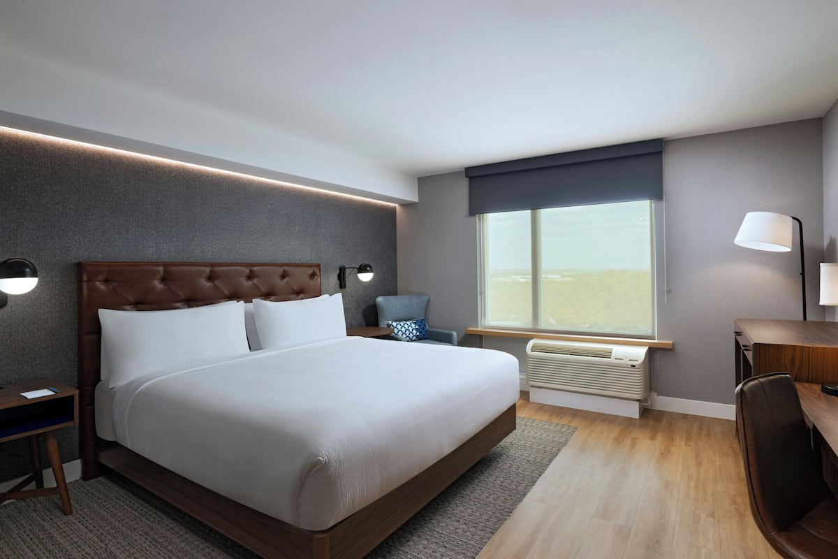 A modern hotel room with a large bed, bedside lamps, a desk, and a window with a view.