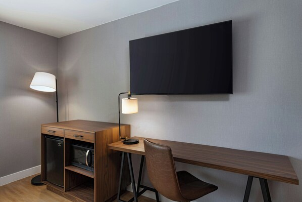 A compact room with a wooden desk, a microwave, a refrigerator, a flat-screen TV, and a lamp. - Four Points BY Sheraton Austin Airport (Austin)