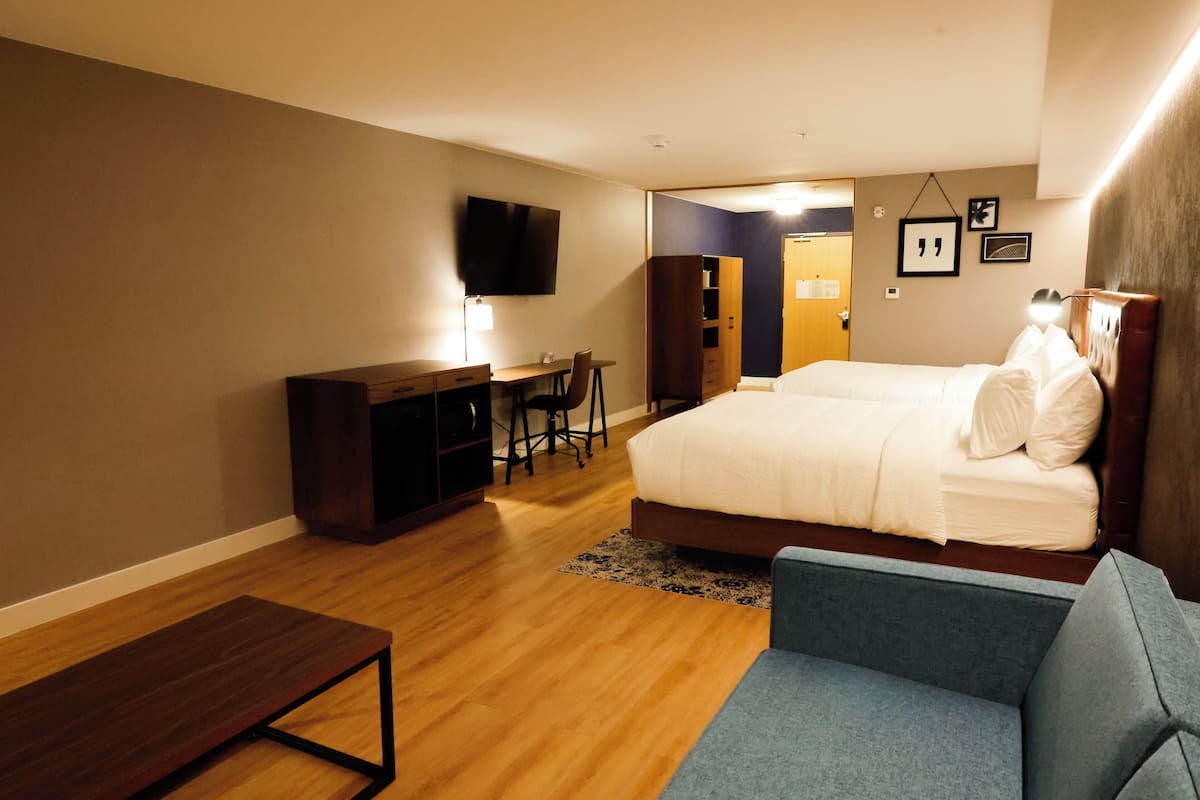 A hotel room with a bed, a desk, a chair, a TV, and a sofa.