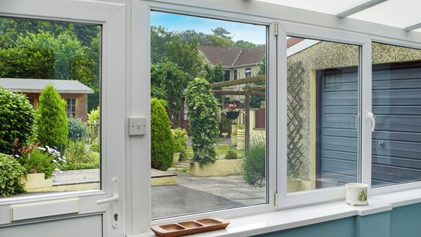 Een kamer met een groot raam, uitzicht op een tuin en omliggende huizen.
