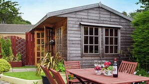 Een houten hut met een veranda, een eettafel met stoelen en een fles wijn.