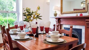 Een eettafel gedekt voor vier personen, met rode en witte servetten, een vaas met gele bloemen en een spiegel boven de open haard.