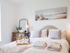 A neatly made bed with pillows, a bedside table with a lamp, a painting, and a tray with cups and a teapot. - 4 bedroom accommodation in Pwll near Llanelli (Pwll near Llanelli)