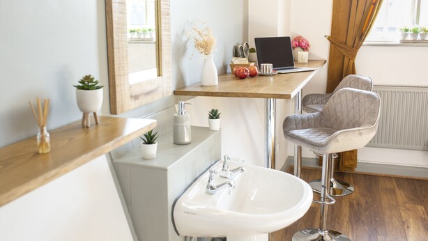A modern bathroom with a wooden vanity, a white sink, a mirror, and a laptop on a small table. - Cades Accommodation (Wolverhampton)