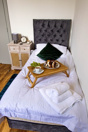 A neatly made bed with a tray of breakfast items, a bedside table with a lamp and clock, and a wooden nightstand with a lamp. - Cades Accommodation (Wolverhampton)