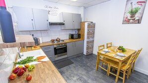 A compact kitchen with a dining area, featuring a wooden table, chairs, and a refrigerator. - Cades Accommodation (Wolverhampton)