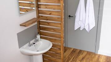 A bathroom with a wooden slatted partition, a white sink, and a grey door with two white towels hanging on a hook.