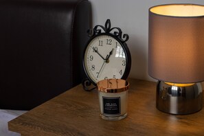 A wooden table with a scented candle, a lamp, and a clock. - Cades Accommodation (Wolverhampton)