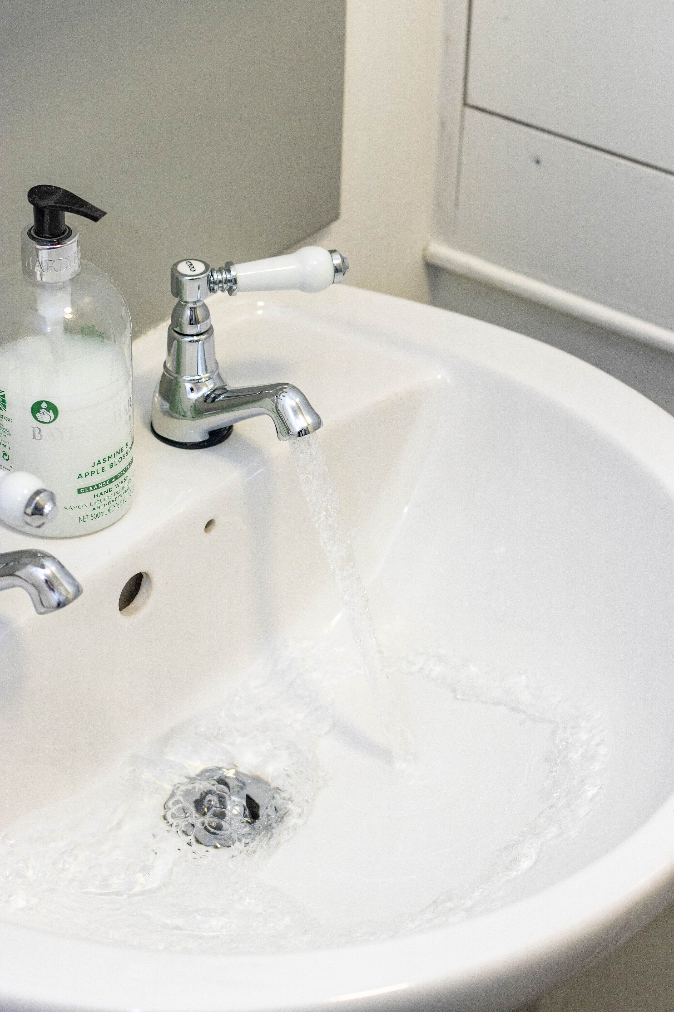 Un lavabo blanc dans une salle de bain, avec de l’eau qui coule, un distributeur de savon et un robinet.